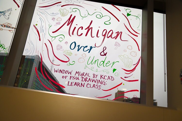 Students in a Kendal College of Art and Design drawing class created a window mural using window paint markers., titled 'Michigan Over and Under,' the piece celebrates Michigan's nature.