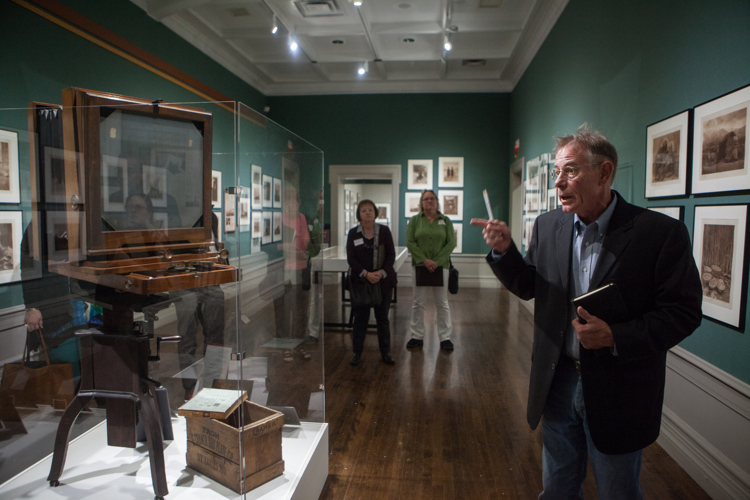 Curator Ben Mitchell points to a camera and other artifacts that accompany the photography exhibition. 