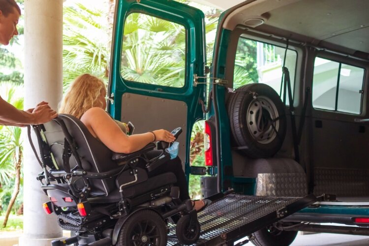 Photo shows a woman using a wheelchair being pushed up a ramp into an accessible van. 