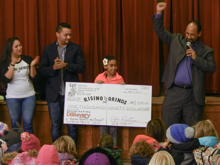 Tayden Beene holds the check for Rising Grinds as Nathan Beene and Principal John Robinson look on.