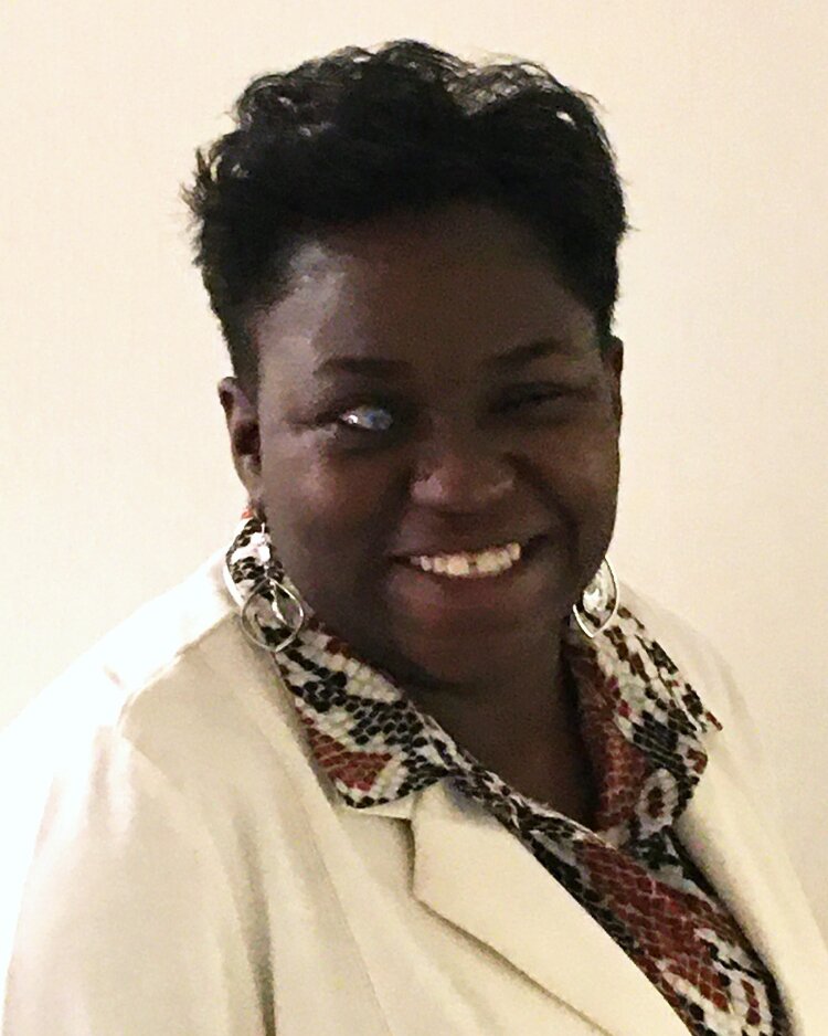 This is a picture of Leatrice Fullerton, a Black woman with short black hair wearing dangling silver earrings, a snake-skin printed blouse, and a cream jacket.