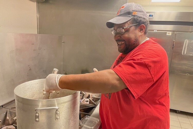 John Capers smiling while stirring his sauce.