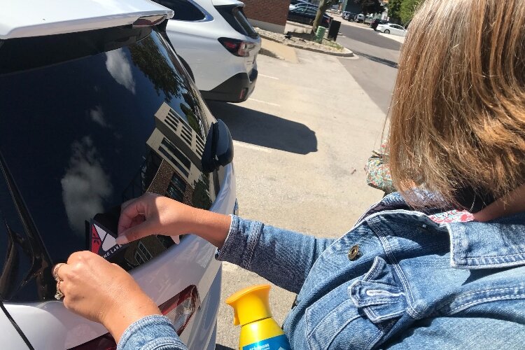 Christine Burns, Village of Spring Lake Manager, puts a sticker of the community's new logo on her car. 